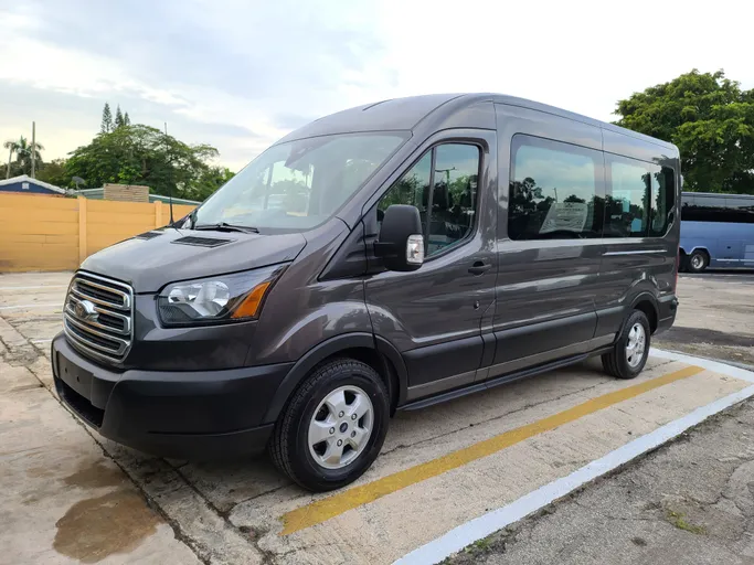 Gray Ford transit van parked in a lot, showcasing its spacious design and modern features, suitable for group transportation needs.