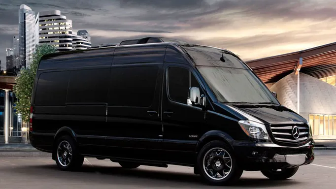Luxury black Mercedes van parked in an urban setting, showcasing its spacious design against a modern city backdrop. Ideal for high-end transport.