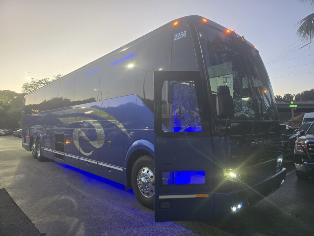 Blue charter bus with illuminated features parked in a lot at dusk, showcasing its sleek design and prominent branding.