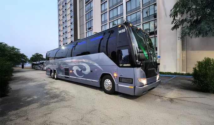 A sleek gray charter bus parked beside a high-rise building, showcasing its modern design and readiness for passenger transport.