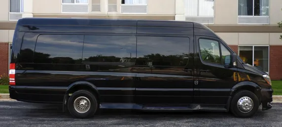 Black passenger van parked beside a hotel. The vehicle's large size suggests it is designed for group transportation.
