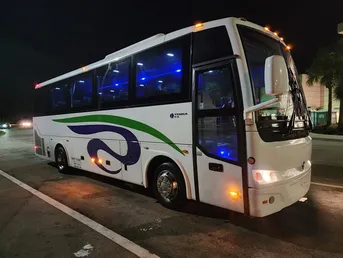 Modern white bus with blue and green accents parked at night, showcasing its illuminated interior. Relevant for transportation or travel services.