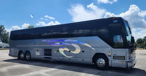 Silver tour bus with a sleek design parked under a clear blue sky, showcasing its modern features and spacious build.