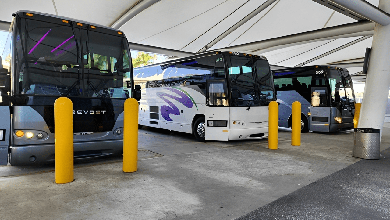Three tour buses parked under a canopy, with yellow poles providing safety barriers. This image highlights bus transport options at a travel hub.