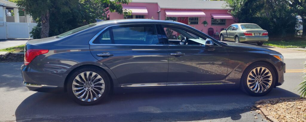 A sleek gray luxury sedan parked on a residential street, showcasing its stylish design and polished rims, with pink-hued houses in the background.
