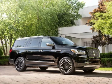 Black luxury SUV parked in a landscaped area, showcasing its sleek design and distinctive alloy wheels, highlighting sophistication and style.
