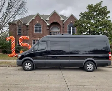 A black van is parked in front of a large brick house, decorated with balloon numbers "15," suggesting a celebration or event.