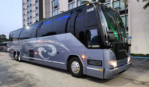 A large gray tour bus parked outside a hotel, featuring sleek design elements and the number 1456 displayed prominently.