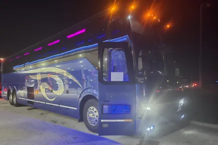 A modern bus with vibrant blue and purple lighting, parked at night. It showcases a sleek design, highlighting its luxury transport features.
